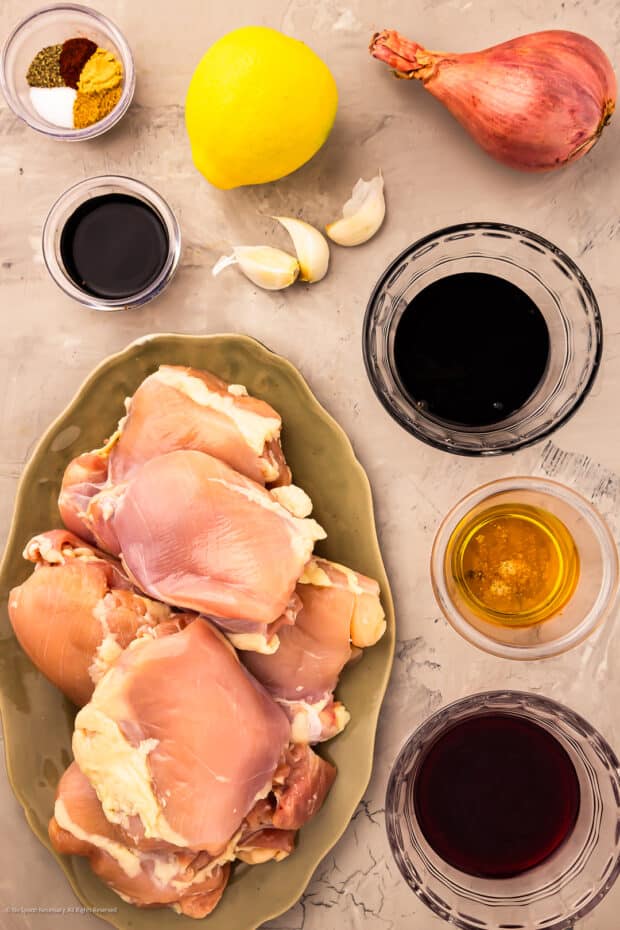 Overhead photo of raw chicken thighs and the ingredients for pomegranate sauce neatly organized on a kitchen counter.
