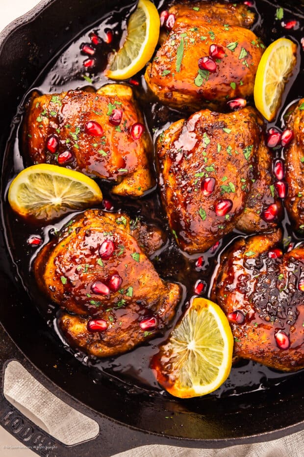Overhead photo of a black skillet containing chicken with pomegranate sauce.