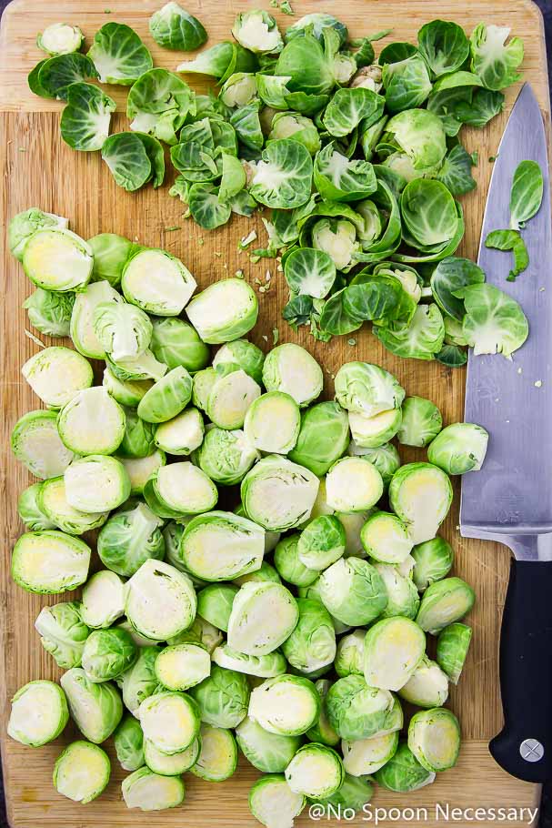 Overhead shot of trimmed and halved brussels sprouts on a cutting board with a knife