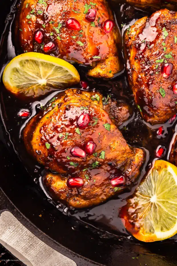 Close-up photo of a pomegranate molasses chicken thigh garnished with pomegranate arils and fresh parsley.