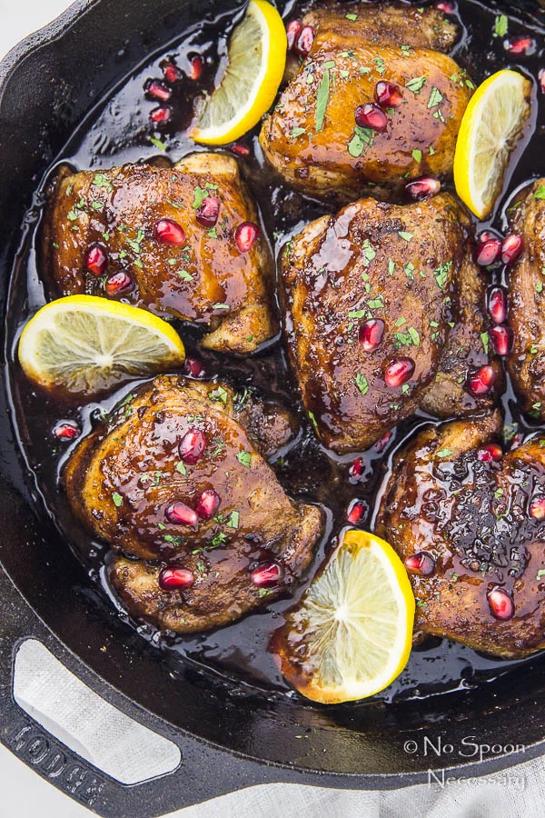 Overhead shot of Skillet Honey Pomegranate Chicken Thighs in a cast iron skillet with lemon wedges and pomegranate arils. 