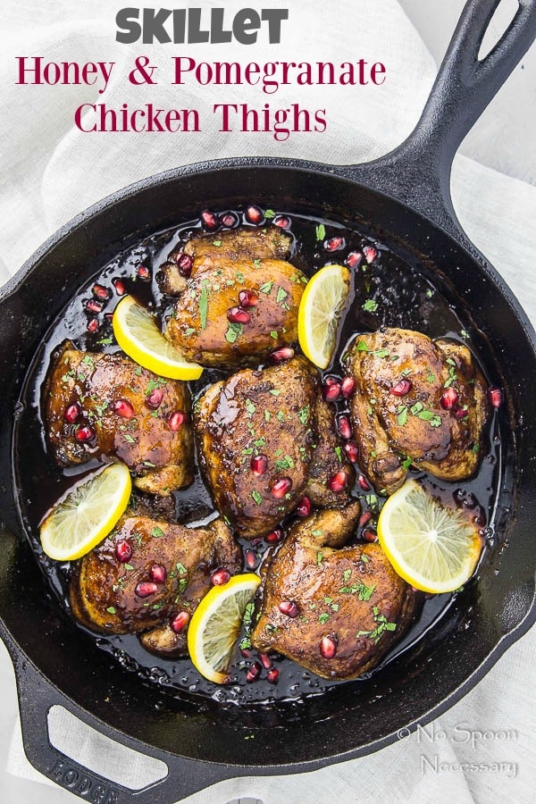 Overhead shot of Skillet Honey Pomegranate Chicken Thighs in a cast iron skillet with lemon wedges and pomegranate arils with a light neutral linen under the skillet.