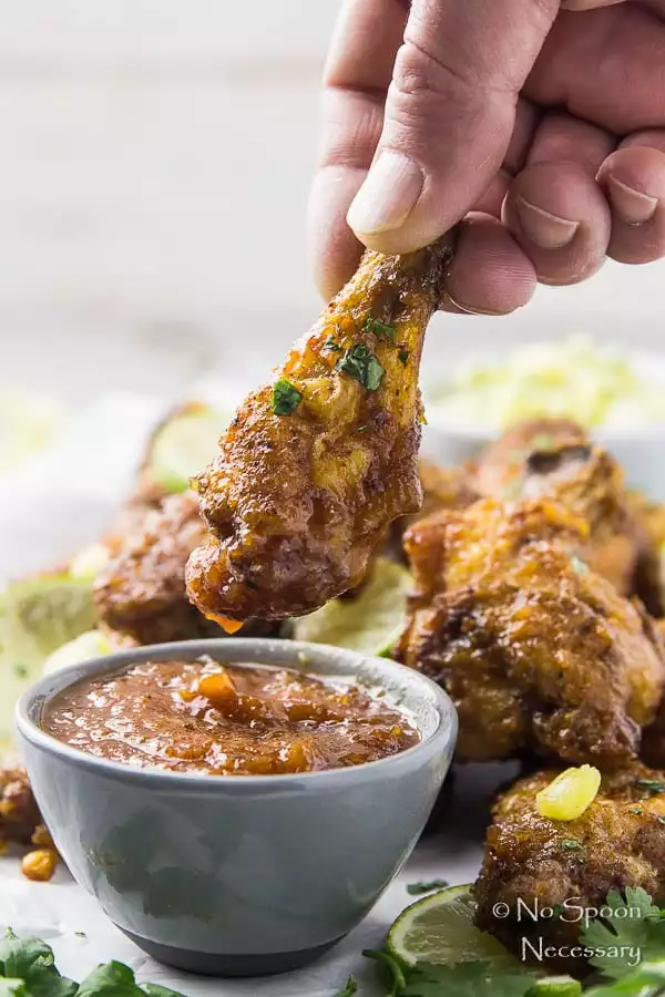 Straight on shot of a hand dunking a Crispy Baked Cajun Chicken Wing into a small ramekin of Honey Chipotle Sauce with more wings blurred behind the bowl.