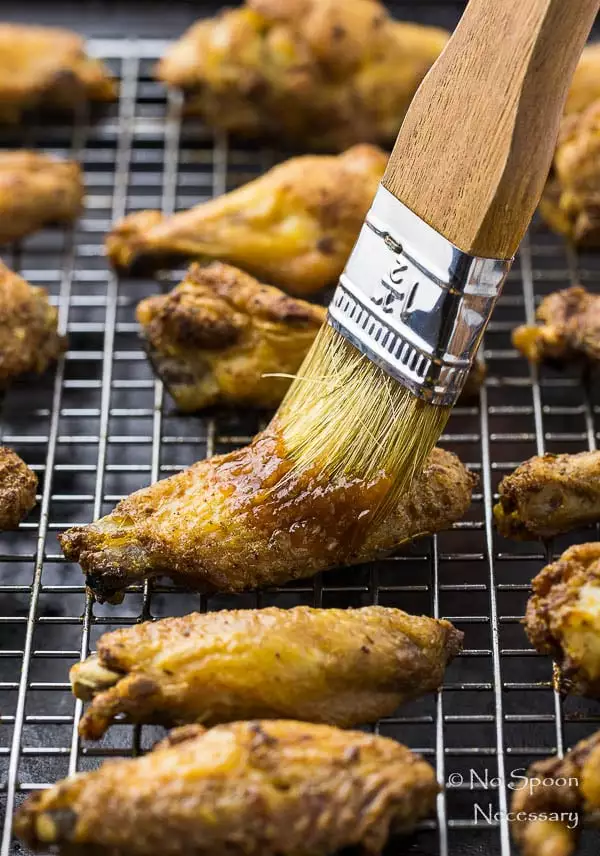 45 degree angle shot of Crispy Baked Cajun Chicken Wings on a wire rack lined baking sheet with a large grill brush applying glaze to the wings.