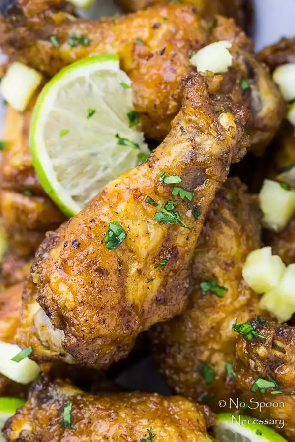Overhead, up-close shot of a Baked Crispy Cajun Chicken Wing garnished with pineapple salsa and slices of lime