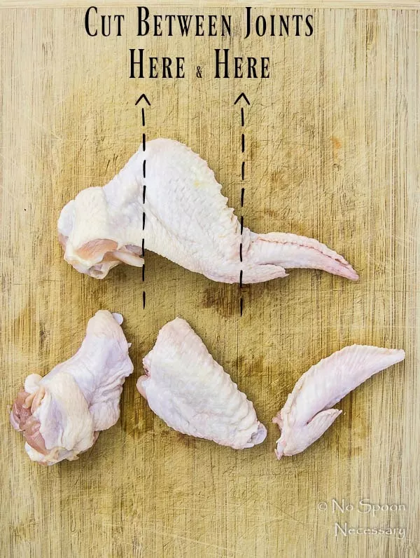 Overhead shot of 2 chicken wings on a cutting board - one whole wing and the other wing is cut between the joints, showing how to prepare chicken wings for cooking.