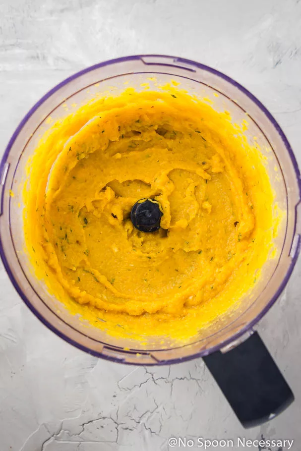 Overhead shot of roasted butternut squash puree in a the bowl of a large food processor sitting on a grayish white counter