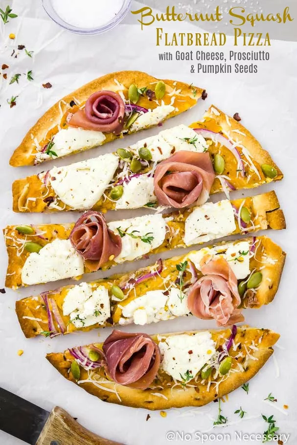 Butternut Squash Flatbread Pizza with Goat Cheese, Prosciutto & Pumpkin Seeds cut into long horizontal slices on a crinkled piece of parchment paper