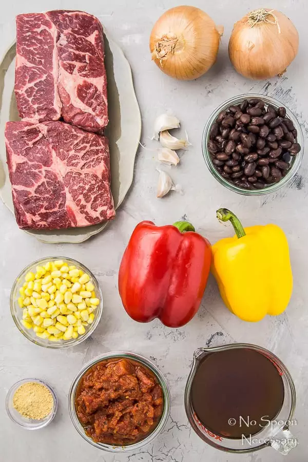Overhead shot of all the ingredients needed to make Slow Cooker Beef Fajita Soup neatly arranged on a gray surface.