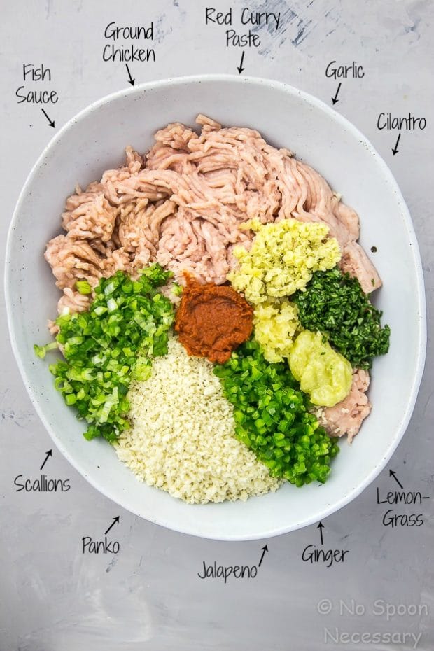 Overhead shot of a neutral colored pottery bowl filled with all the ingredients to make Sticky Baked Thai Chicken Meatballs neatly organized, with the name of each ingredient written on the photo and pointing to each individual ingredient.