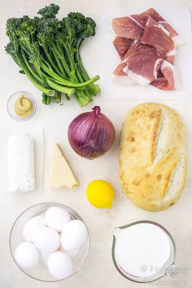 Overhead shot of all the ingredients to make Overnight Broccolini & Goat Cheese Strata with Crispy Prosciutto neatly organized on a pale beige surface.