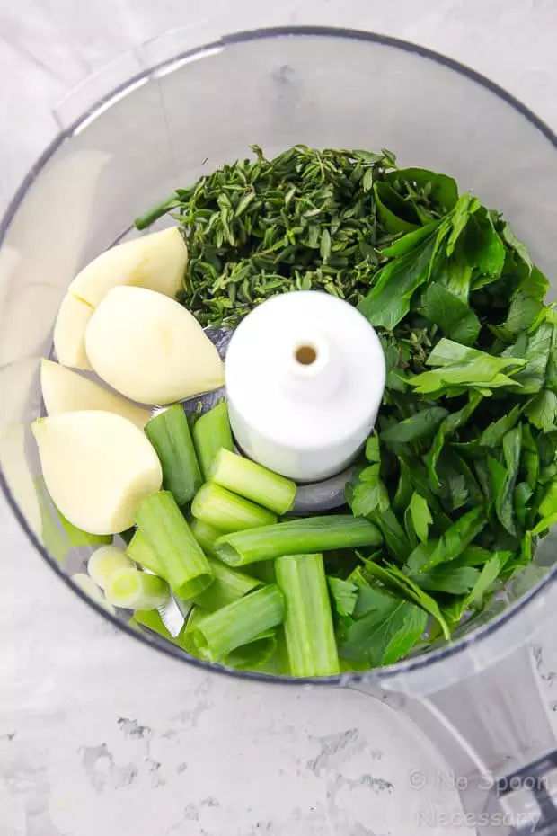 Overhead shot of the inside of a food processor bowl filled with the ingredients needed to make Gremolata, which is the garnish for Garlic & Herb Pork Chops recipe. 