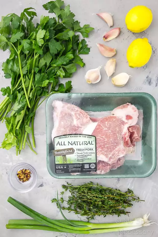 Overhead shot of all the ingredients needed to make Garlic & Herb Pork Chops with Gremolata recipe neatly organized on a gray surface.