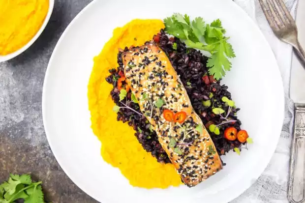 Overhead, landscape shot of Honey Sesame Salmon & Asian Black Rice Salad with carrot-ginger sauce on a white plate garnished with fresh cilantro.