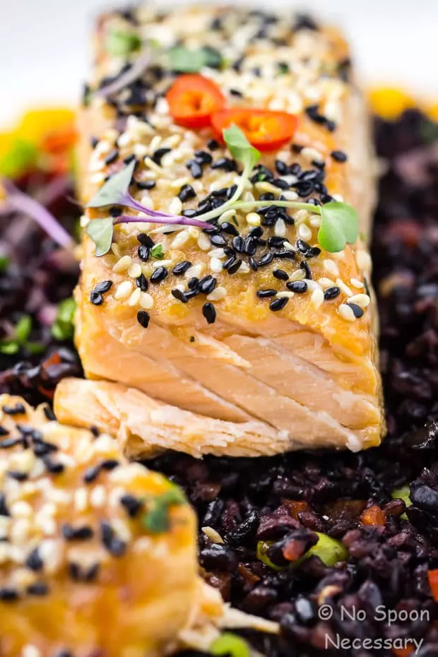 Angled, extreme up close shot of cut into Honey Sesame Salmon served on top of Asian Black Rice Salad.