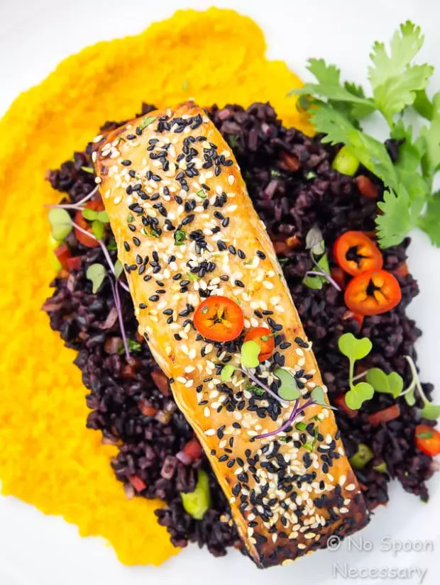 Overhead, up close shot of Honey Sesame Salmon & Asian Black Rice Salad with carrot-ginger sauce on a white plate garnished with fresh cilantro.