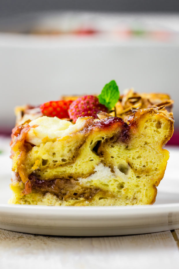 Straight on, up-close shot of a square slice of Overnight Strawberry Ricotta Breakfast Strata on a white plate.