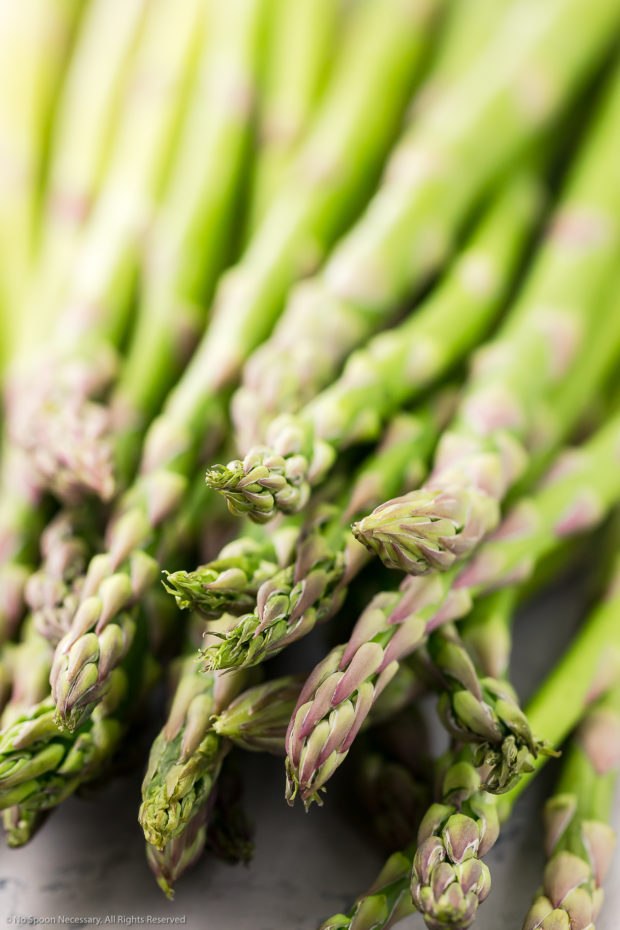 Angled, up close photo of a bundle of raw asparagus spears - one of the vegetables in couscous recipe.