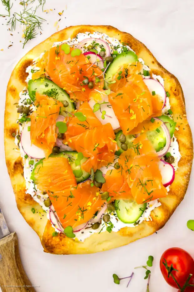 Photo of baked pizza topped with cream cheese, salmon and veggies.
