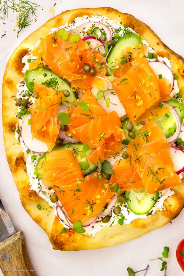 Overhead photo of smoked salmon on pizza with cream cheese, capers and cucumbers.