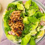Overhead photo of a green salad with peas and grilled chicken breast on a dinner plate.