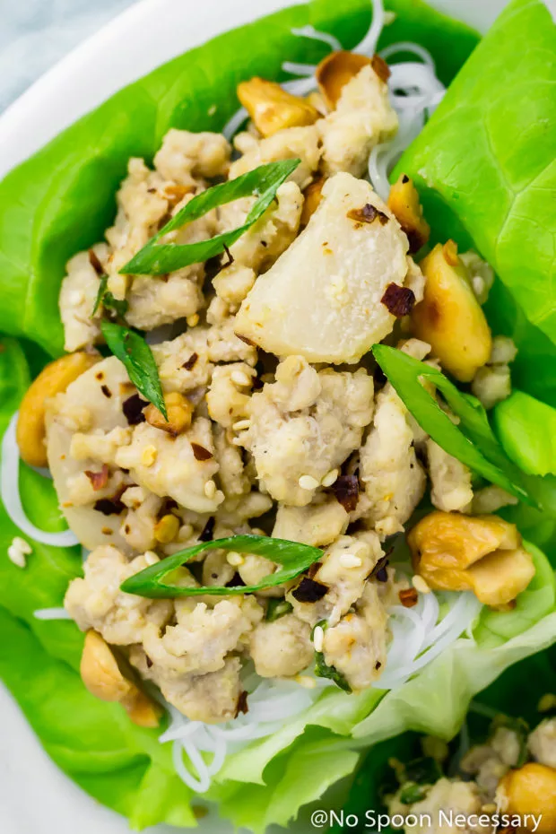 Overhead, extreme close up shot of Cashew Chicken Lettuce Wraps on a white platter, with the focus on the chicken filling in the wrap.