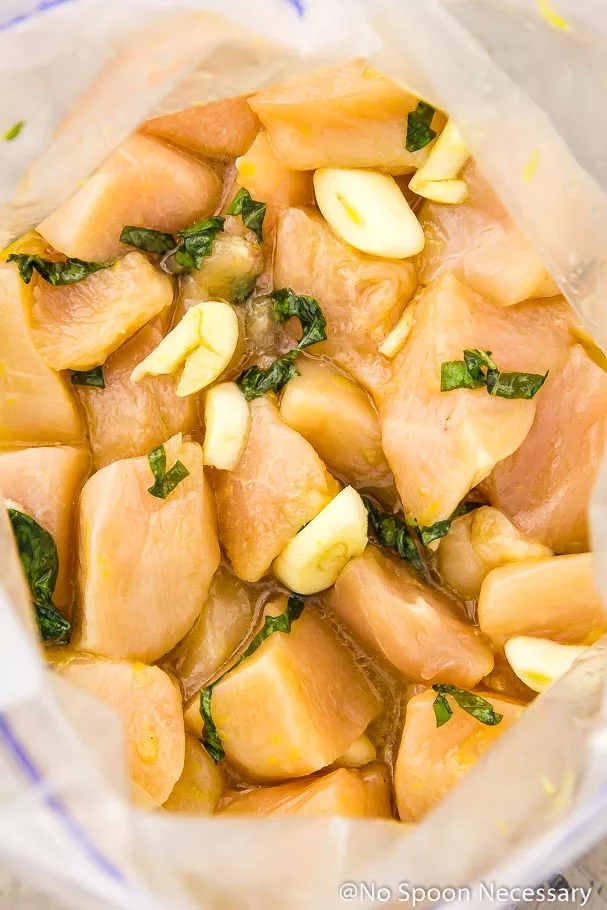 Cubes of chicken with slivers of garlic and basil marinating in a zip-closure bag