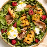 Overhead photo of a grilled peach salad with burrata, prosciutto and berries.