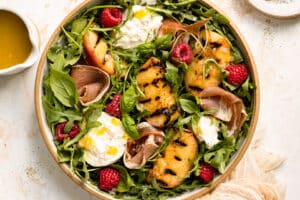 Overhead photo of a grilled peach salad with burrata, prosciutto and berries.