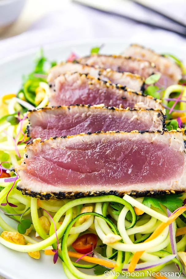 Angled, up-close shot of rare, spicy sesame crusted, pan seared tuna slices over a bed of Thai zucchini noodles