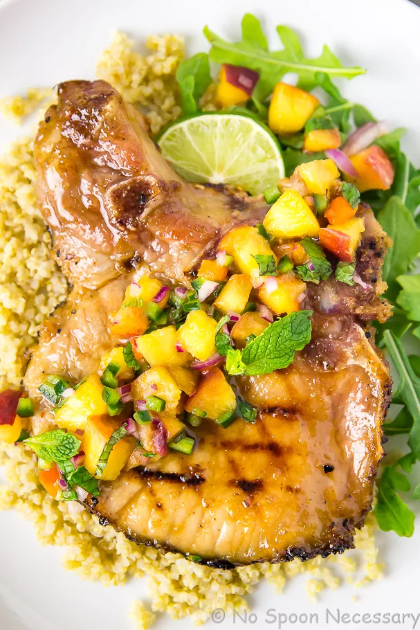 Overhead shot of Ginger Honey Glazed Pork Chops with Peach-Poblano Salsa on quinoa and arugula with a lime wedge.