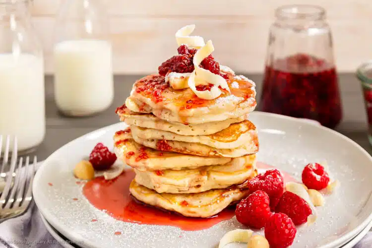 Straight on photo of a stack of Hawaiian pancakes with fruit and maple syrup.