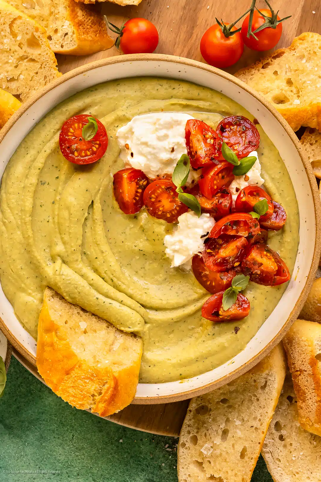 Overhead photo of a piece of toast dipped into a bowl of hummus made with fresh herbs.