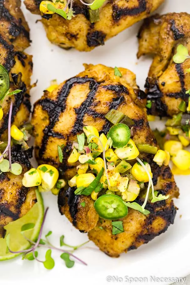 Overhead, up-close shot of a Southwest Buttermilk Grilled Chicken Thigh topped with Corn Salsa, sliced jalapenos and microgreens