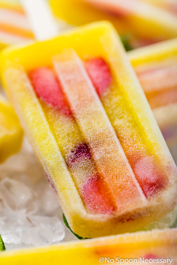 Up close, angled shot of Strawberry Mango Gin and Tonic Boozy Popsicles on a surface of crushed ice. 