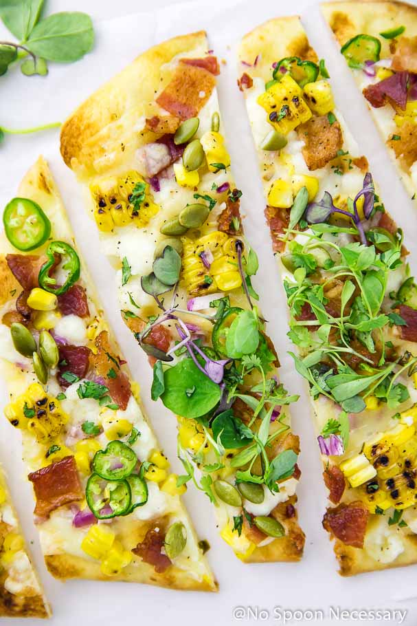 Overhead shot of 3 slices of Tex-Mex Charred Corn, Bacon & Jalapeno Pizza on a white board with a microgreen in the top left corner