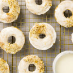 Overhead shot of Baked Apple Cider Donuts on a a gold wire rack with a ramekin of glaze tucked into the corner of the shot.