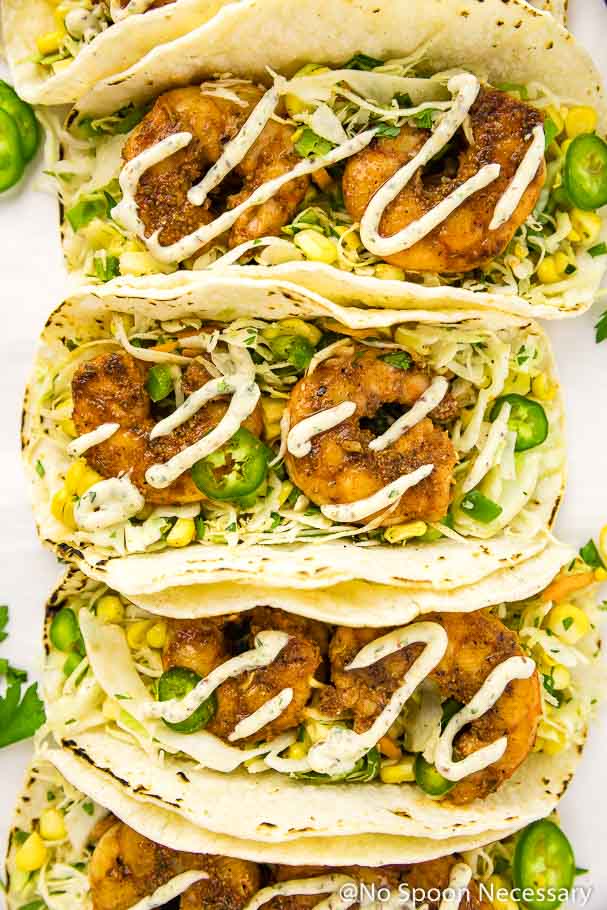 Overhead shot of row of Cajun Shrimp Tacos with spicy corn slaw drizzled with remoulade on a white board.
