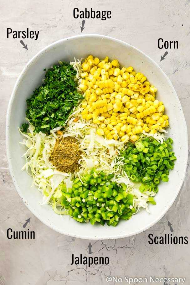 Overhead shot of the ingredients for spicy corn slaw in a neutral bowl with the ingredient name written out and an arrow pointing to each ingredient - one of the main components to make Cajun Shrimp Tacos.