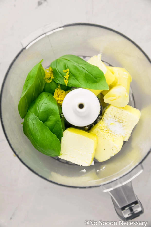 Overhead shot of the ingredients to make Basil Butter in the bowl of a food processor.
