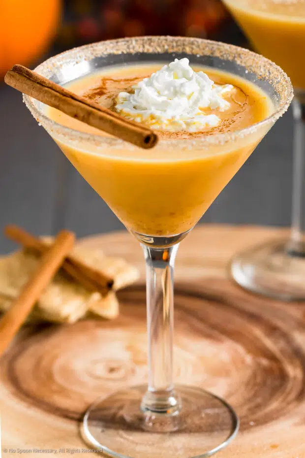 Straight on photo of a pumpkin pie martini topped with whipped cream, ground cinnamon and a cinnamon stick.