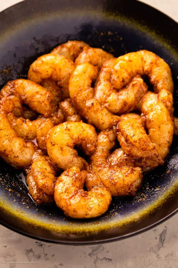 Photo of raw shrimp with blackening seasoning in a mixing bowl.