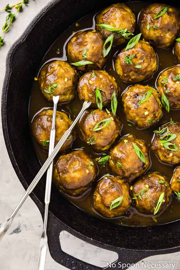 Overhead shot of Baked Chicken Apple Meatballs in a cast iron skillet with large silver skewers inserted into two meatballs