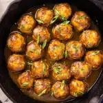 Overhead photo of chicken apple meatballs garnished with sliced green onions in a cast iron skillet.
