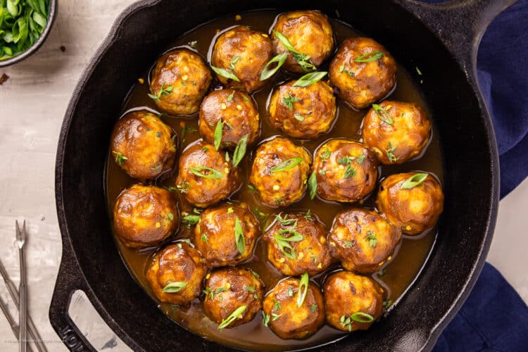 Overhead photo of chicken apple meatballs garnished with sliced green onions in a cast iron skillet.