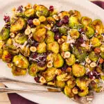 Overhead photo of maple brussels sprouts with cranberries and hazelnuts on a white serving platter.
