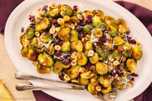 Overhead photo of maple brussels sprouts with cranberries and hazelnuts on a white serving platter.