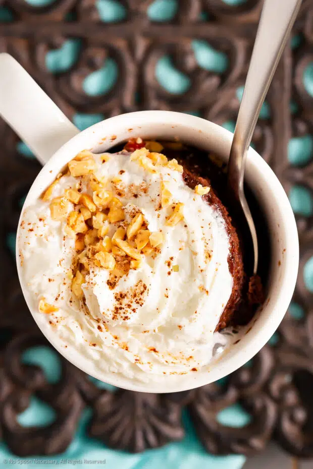 Overhead photo of a spoon digging into a chocolate lava mug cake topped with whipped cream, chopped nuts, and cocoa powder.