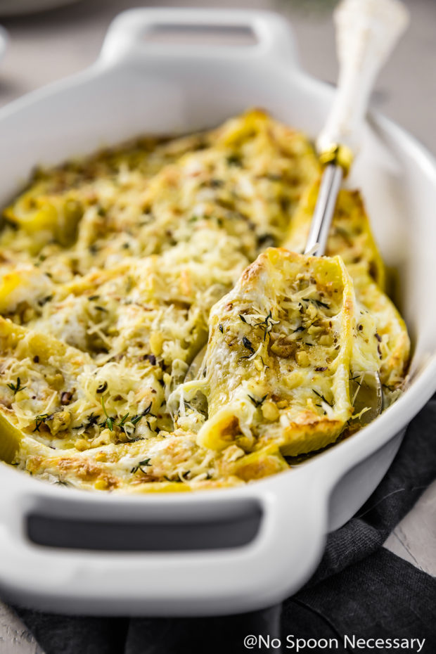 Angled shot of Baked Pumpkin Stuffed Shells topped with Parmesan in a white baking dish with a white handled silver serving spoon tucked underneath and lifting up one of the shells.