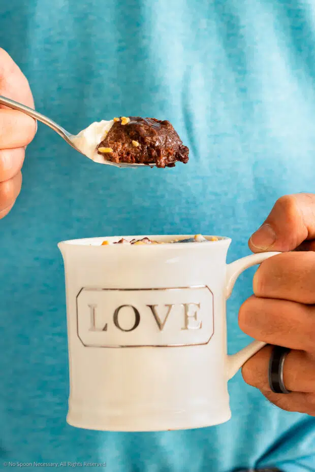 Straight on photo of a person eating a chocolava cake out of a white coffee mug. 